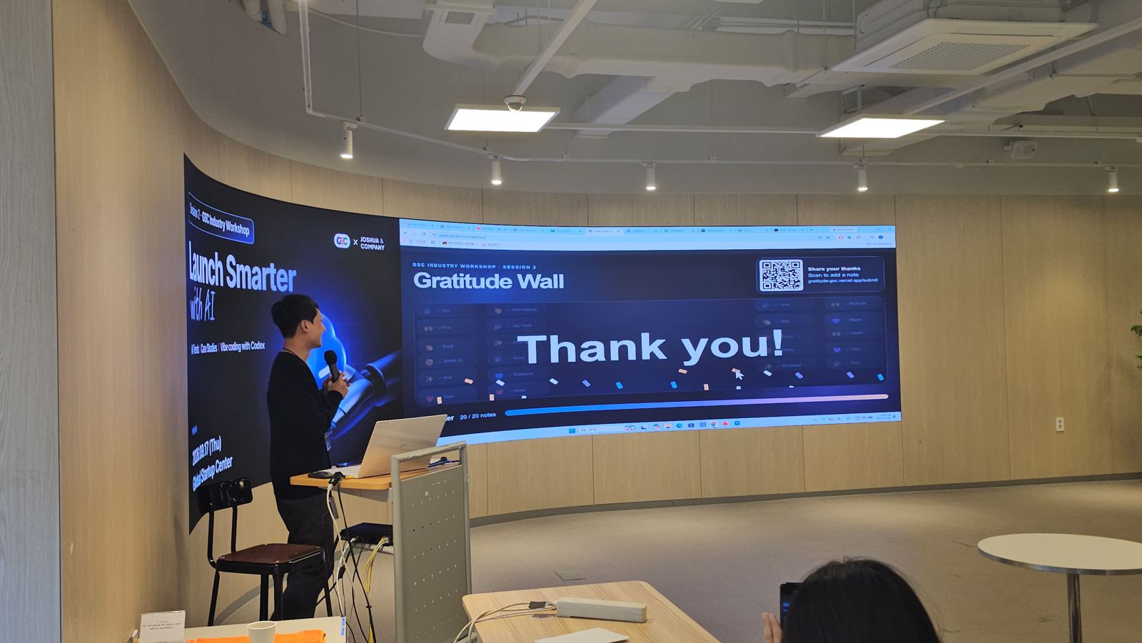 Gratitude Wall 화면에 'Thank you!'가 크게 떠 있고 발표자가 마이크를 들고 서 있다